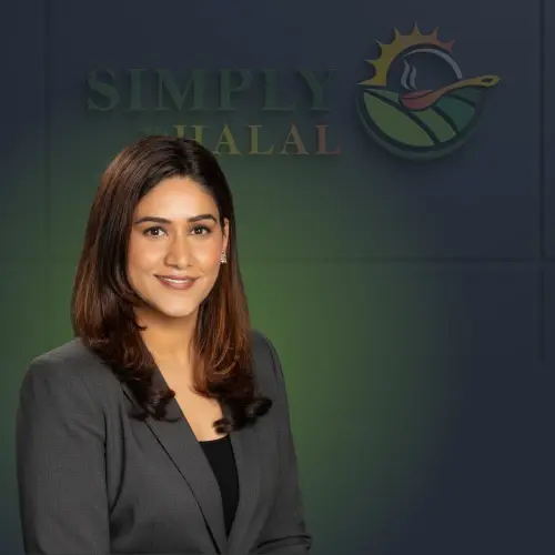 Professional portrait of a smiling woman in a dark blazer, standing in front of the Simply Halal logo background.